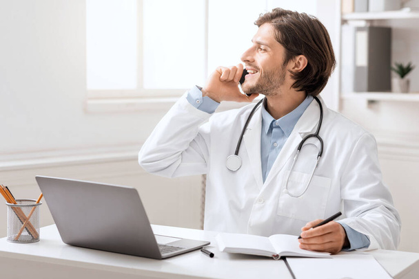 若い医者はオフィスで携帯電話で患者と話す - 写真・画像