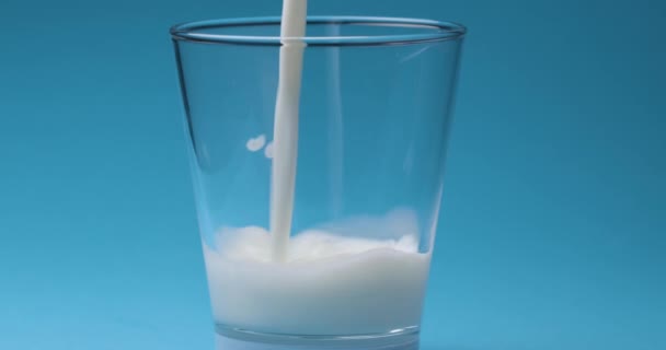 Milk is poured into a milk glass on a blue background. - Filmati, video