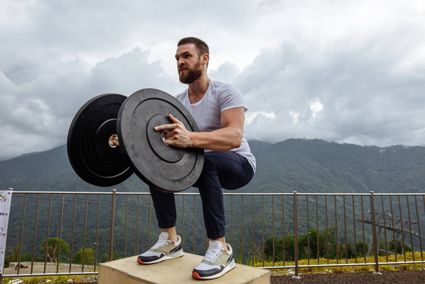 Strong male athlete doing box jumps with two plates outdoor on top of mountain. - Фото, изображение