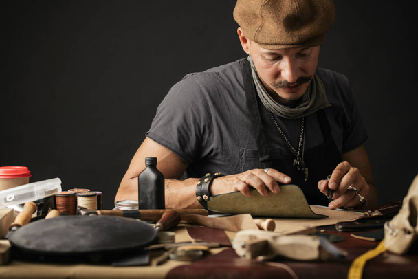 Whiskered shoemaker with making measurments in patterns at table in workshop - 写真・画像