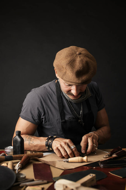 Whiskered shoemaker with making measurments in patterns at table in workshop - Fotografie, Obrázek