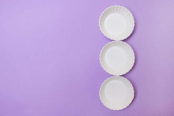 tres plato blanco vacío sobre fondo de papel de color púrpura con espacio de copia
. - Foto, Imagen