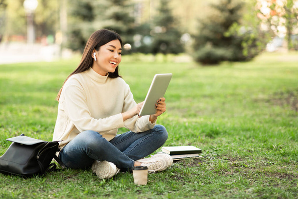 Студент за планшетом, сидит в парке - Фото, изображение