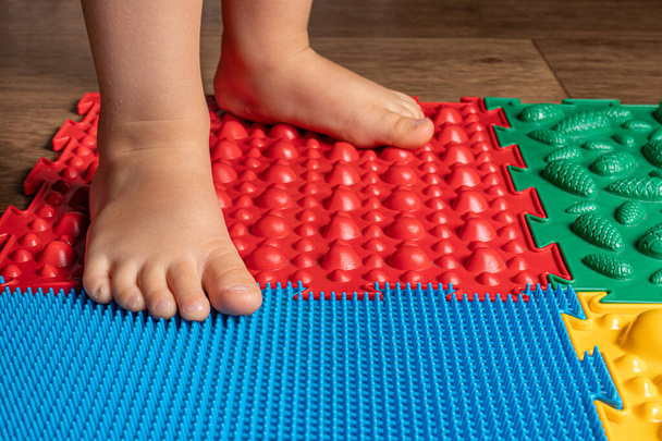 Las piernas de un niño pequeño en alfombras ortopédicas. Superficies brillantes para caminar y formar el arco correcto del pie. Masaje rompecabezas estera. - Foto, Imagen
