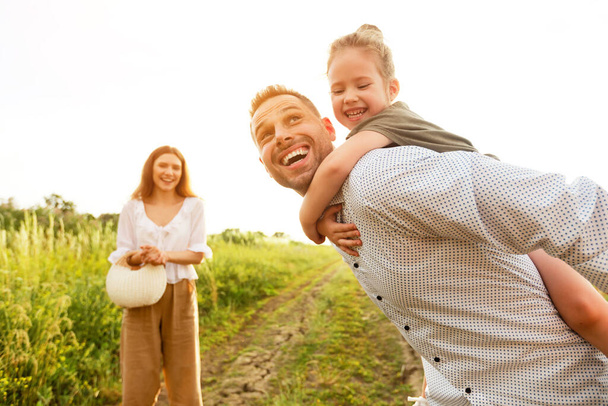 Cheerful dad piggybacking his little baby in countryside - Photo, Image