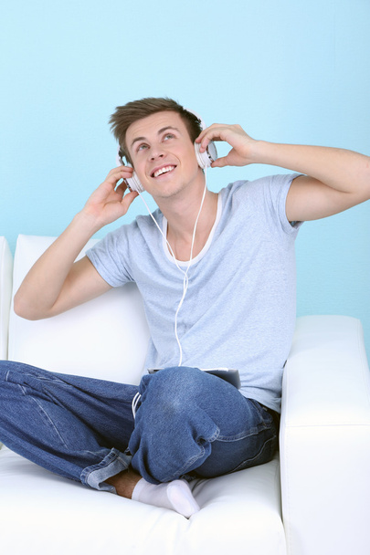 Guy sitting on sofa and listening to music on blue background - Foto, afbeelding