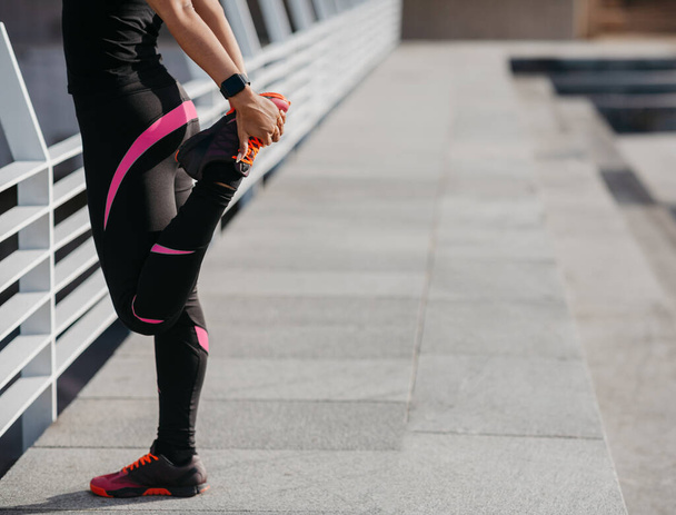 Красивое тело и тренировка. Девушка в спортивной форме делает упражнения для ног в городе, на открытом воздухе - Фото, изображение