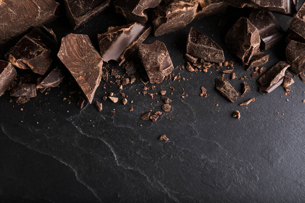 Pieces of dark chocolate on black table, flat lay - 写真・画像