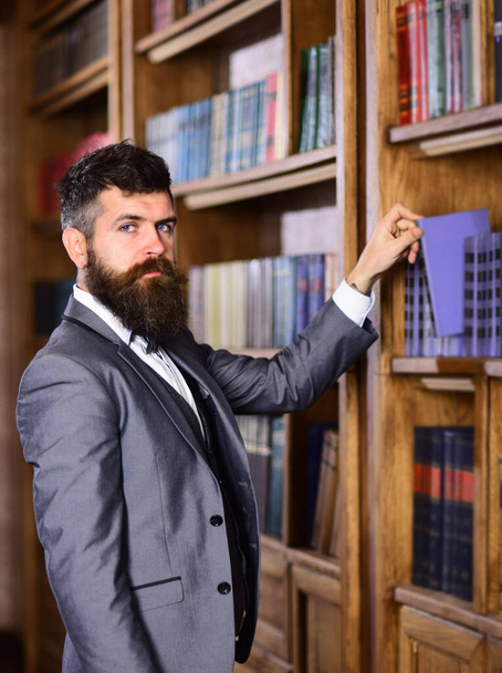Writer holds book in vintage library. Mature man with serious face and long beard. - Foto, Imagen