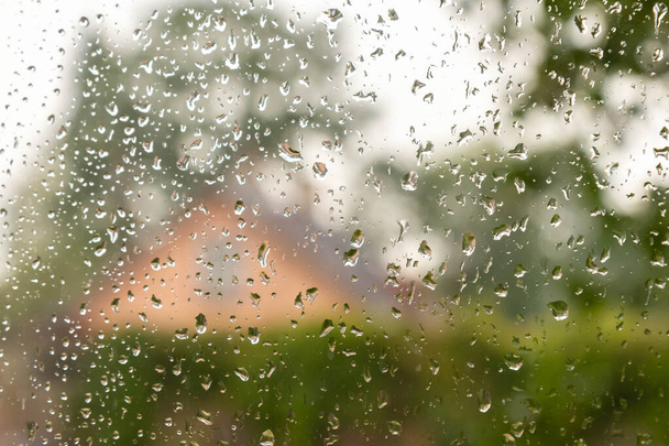 窓に水が落ちる。窓ガラスに雨滴を介して秋の田園風景。背景のぼやけたガラスの上に雨の滴。カントリーハウスの湿式ガラス窓。選択的焦点. - 写真・画像