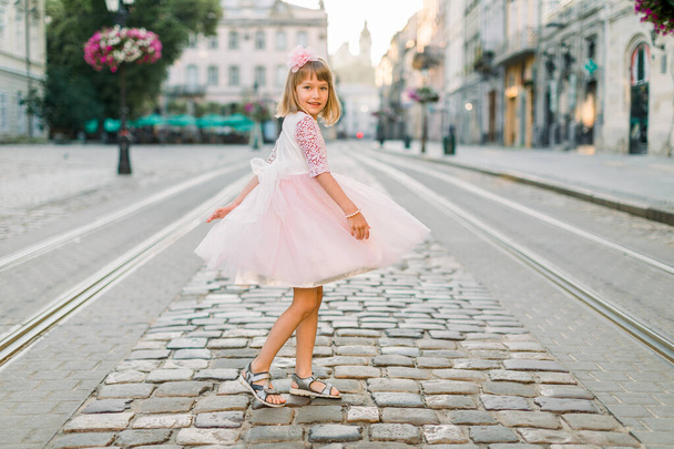 Little girl in pink dress and flower in her hair walking through the streets of the old town in Lviv, Ukraine - Фото, зображення