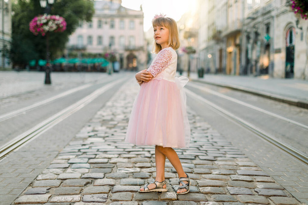 Маленька дівчинка в рожевій сукні принцеси виходить на вулицю і насолоджується видом на стародавній європейський центр міста. Життєпис маленької дівчинки, що ходить по місту. - Фото, зображення