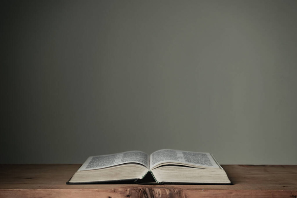 Otevřete Bibli svatou na červeném dřevěném stole a bílém pozadí zdi. Náboženský koncept. - Fotografie, Obrázek