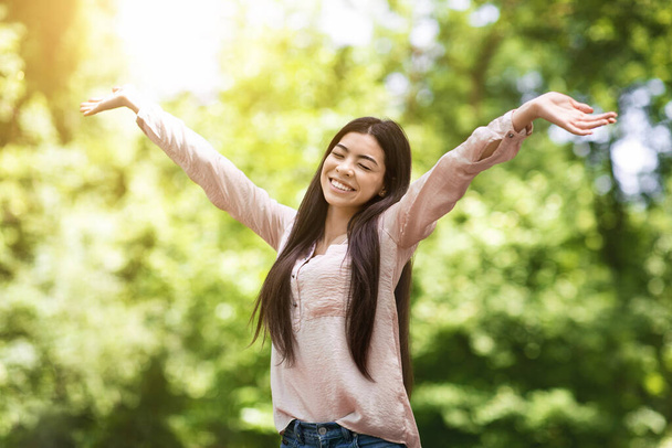 Kocham życie. Azjatycka dziewczyna szczerze uśmiechnięta i podnoszące ręce w parku - Zdjęcie, obraz
