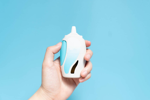 Hand hält Steroid Nasenspray Suspension mit leerem Etikett auf hellblauem Hintergrund. Medizinprodukt zur Behandlung von allergischem Schnupfen, Heuschnupfen, Nasennebenhöhlenentzündung oder Nasenpolypen. Gesundheitskonzept. Nahaufnahme. - Foto, Bild