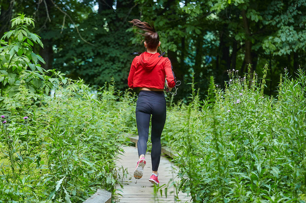 Attractive girl in sportswear jogging along a wooden path in a forest park. - Foto, imagen