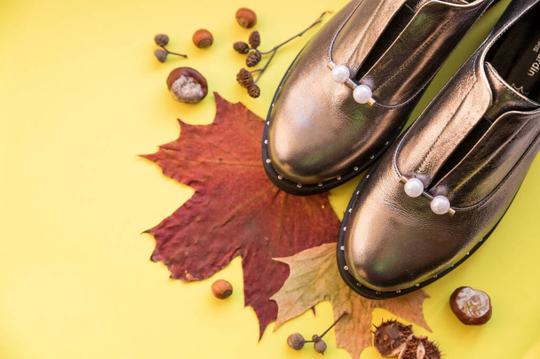 Autumn look with shiny boots on yellow background. concept Autumn, fashion composition. Casual boots with fallen leaves. fall season concept. stylish sneakers with pearls. womens shoes.Copy space - Photo, Image