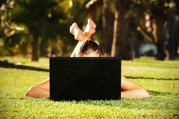 mezítláb nő a fű, vele laptop mögé bújva - Fotó, kép