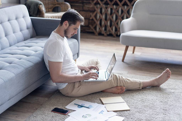 Man working on laptop computer sitting on the floor with his diary and official papers at home - Photo, image