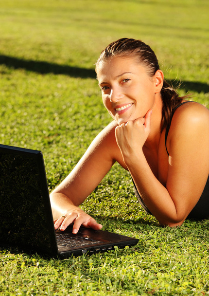 Menina bonita trabalhando em seu laptop na grama
 - Foto, Imagem