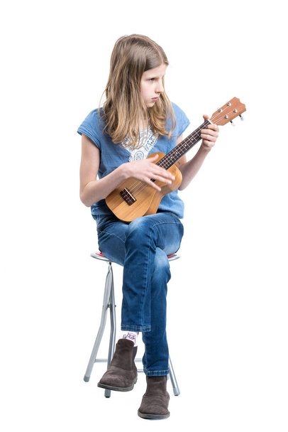 Adolescente, chica rubia en camiseta azul está sentado y tocando concierto en el instrumento ukelele. - Foto, Imagen