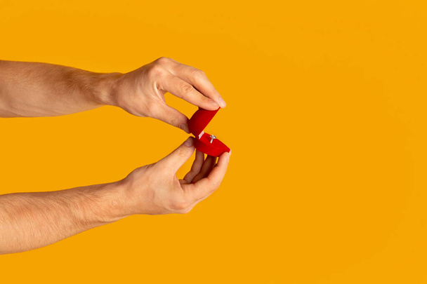 Nahaufnahme von Millennial Guy Öffnung Box mit Verlobungsring auf orangefarbenem Hintergrund, Kopierraum - Foto, Bild