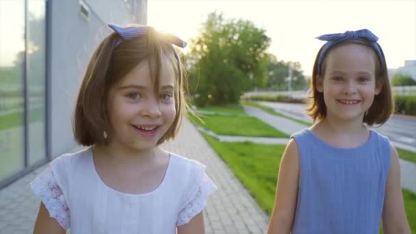 Δύο χαριτωμένα κοριτσάκια περπατούν στους δρόμους της πόλης το ηλιοβασίλεμα. - Πλάνα, βίντεο