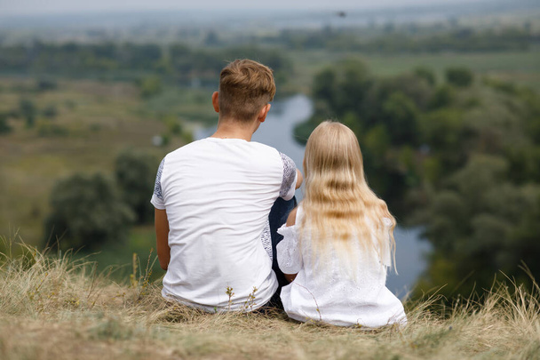 Αγόρι και κορίτσι κάθονται στο λόφο πάνω από το ποτάμι. - Φωτογραφία, εικόνα