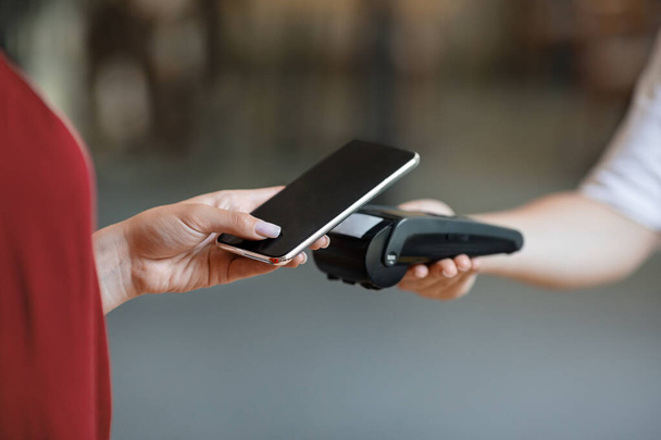 NFC-technologie. Onherkenbare vrouw maiking contactloze betaling met smartphone naar terminal - Foto, afbeelding
