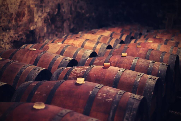 деревянные бочки, сложенные для производства, хранения и выдержки итальянского вина, в темном и прохладном подвале. - Фото, изображение