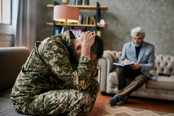 Remove your pain. Middle aged military man holding his head in pain and depression during therapy session with psychologist. Soldier suffering from psychological trauma. PTSD concept - Fotó, kép