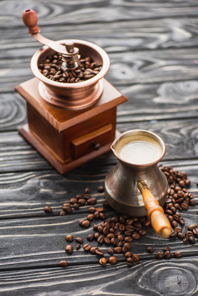 selective focus of vintage coffee grinder with coffee beans near cezve on wooden surface - Photo, Image