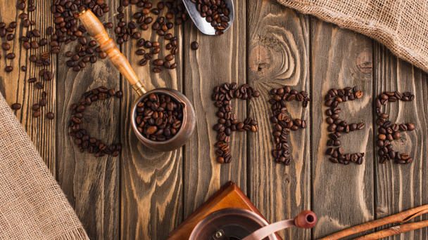 top view of coffee lettering made of beans and cezve on wooden surface - Photo, Image