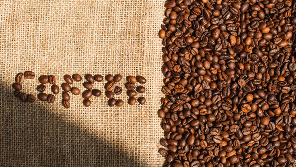 vrchní pohled na kávové písmo z fazolí ve slunečním světle na pytlovině - Fotografie, Obrázek