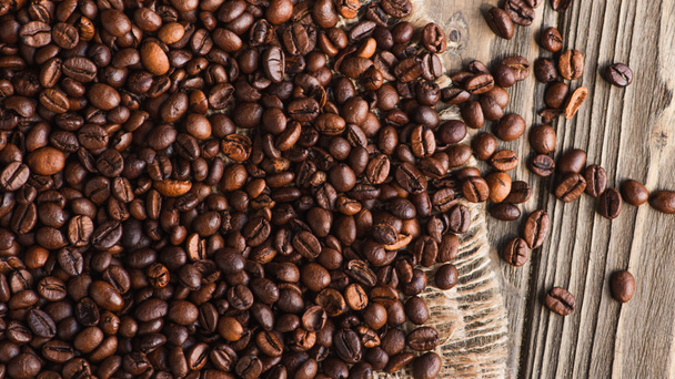 top view of coffee beans scattered on burlap on wooden surface - Foto, Imagen