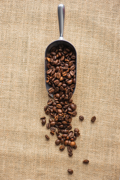vista superior de cucharada de metal con granos de café en tela de saco - Foto, Imagen
