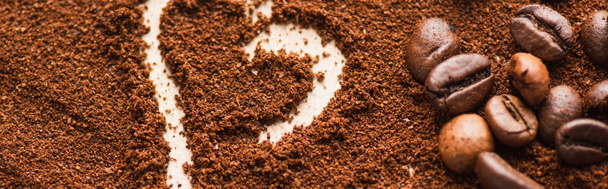 крупный план сердца, нарисованного на молотом кофе рядом с фасолью, панорамный снимок - Фото, изображение