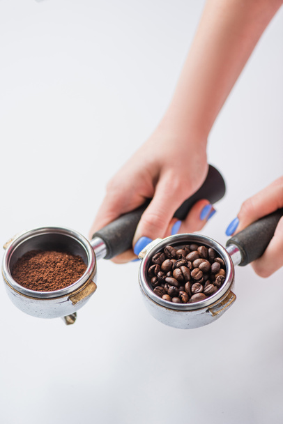 abgeschnittene Ansicht von Barista mit Portafiltern mit Kaffeebohnen und gemahlenem Kaffee auf weißem Hintergrund - Foto, Bild