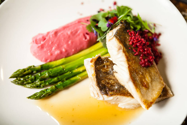 Pike-perch fillet. Asparagus, pearl couscous, white wine sauce, beet-flavored mashed potatoes. Delicious seafood fish closeup served on a table for lunch in modern cuisine gourmet restaurant - Фото, зображення