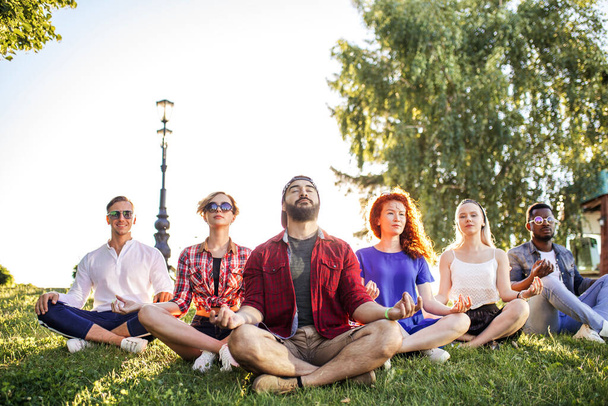 Group of adult mix-race friends meditating while practice yoga outside in park. - Фото, зображення