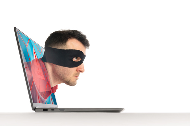 Der Mensch in schwarzer Maske bewegt sich durch den Bildschirm eines Laptops. Konzept von Hacking und Identitätsdiebstahl. Isoliert auf Weiß. - Foto, Bild