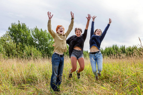 Літні канікули - концепція щасливих людей. Група з трьох друзів хлопчик і дві дівчини стрибають, танцюють і розважаються разом на відкритому повітрі. Пікнік з друзями під час подорожі по природі
 - Фото, зображення
