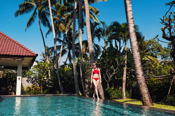 Young woman in red swimsuit standing neat the beautiful swiming pool - Foto, afbeelding