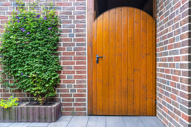 Puerta de jardín de madera cerrada con llave en el interior con mango negro, pared de ladrillo rojo visible
. - Foto, Imagen