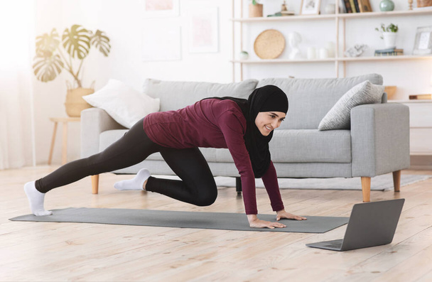 Home Workout. Moslim meisje training in de voorkant van laptop, doen been oefeningen - Foto, afbeelding