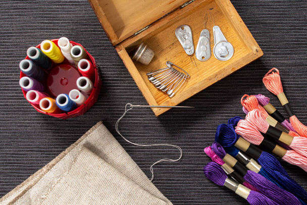 Los accesorios de costura están en una caja de madera. La mulina y los hilos de colores se encuentran en la mesa junto al ataúd. La aguja con el roscado en ella se encuentra en la esquina del ataúd. - Foto, Imagen