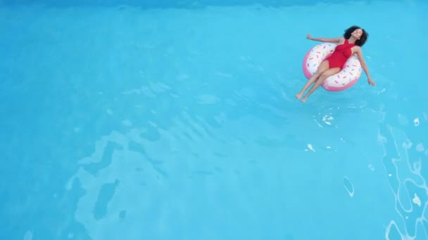 Nur eine Dame, die im aufblasbaren Kreis auf der Sonnenbräune des blauen Wassers schwebt, verbringt ihre Zeit im Ausland in einem tropischen Resort und schießt von oben voll. Afroamerikanische Frau schwimmt Pool in Röhre, Long Shot - Filmmaterial, Video