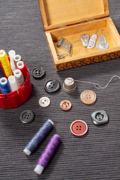 Différents boutons colorés pour les vêtements se trouvent sur la table. Les accessoires de couture sont cousus à côté de vous. Coudre un bouton aux vêtements. L'aiguille avec le fil dessus repose contre le dé à coudre. - Photo, image