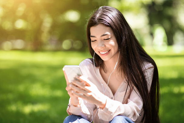 Kedvenc szabadidő. Boldog ázsiai lány hallgat zenét a szabadban okostelefonnal és fülhallgatóval - Fotó, kép