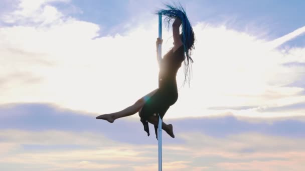 Pool dans op de natuur - vrouw met blauwe vlechten in zwarte jurk vasthouden aan de paal en dansen op de achtergrond van de lucht - Video